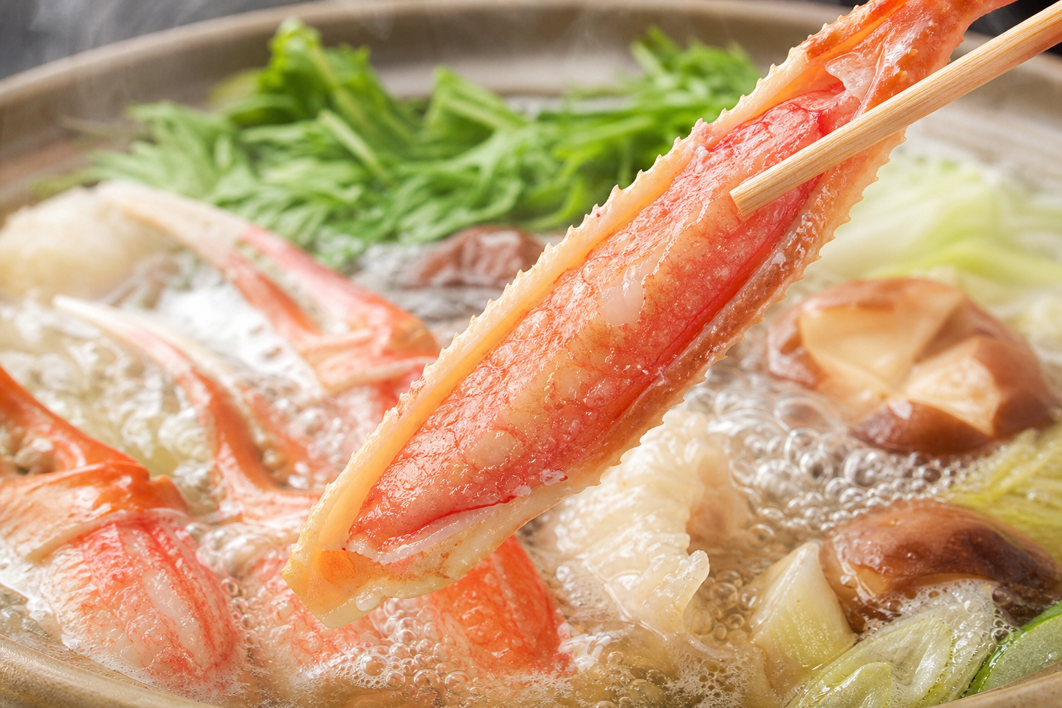 殻の半分が綺麗に剥かれた特大ズワイガニの脚肉(半むき身ポーション)のアップ写真。包丁を使わずにそのままお鍋に入れられる手軽さと、殻から旨味たっぷりのダシが出ている様子を表現した美味しそうなクローズアッ